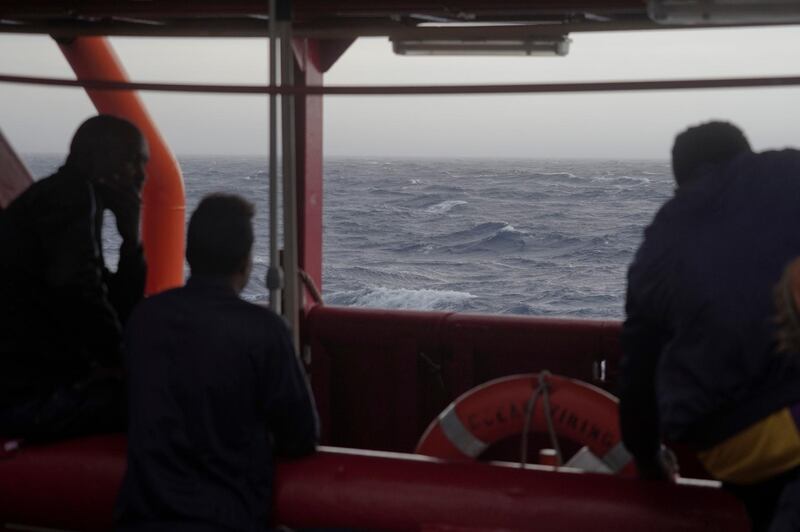 Men look at the rough seas from aboard the Ocean Viking in the Mediterranean Sea, Sunday, Sept. 22, 2019. The humanitarian ship carrying 182 people in international waters is sailing back and forth between Italy and Malta as it waits for European governments to allow it in. (AP Photo/Renata Brito)