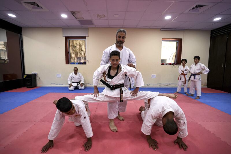 A karate instructor assists a student to perform a split on top of two other students.
