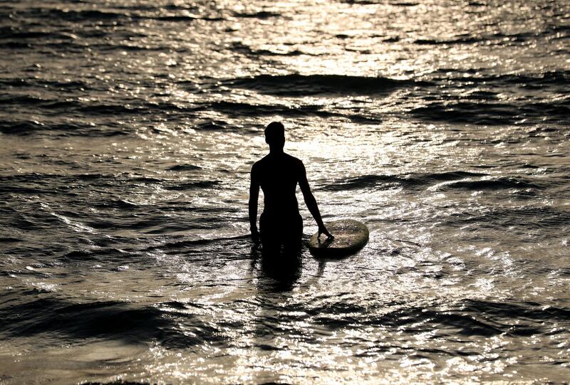 A man heads into the water to surf at sunset in Dubai on June 8th, 2021. Chris Whiteoak / The National. 
Reporter: N/A for News