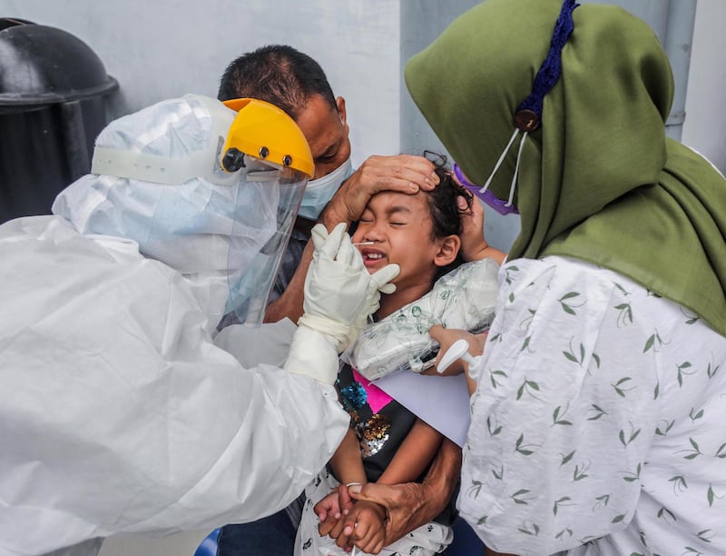 A healthcare worker in a hazmat suit collects swab sample from a girl during a Covid-19 test in Medan, North Sumatra, Indonesia. EPA