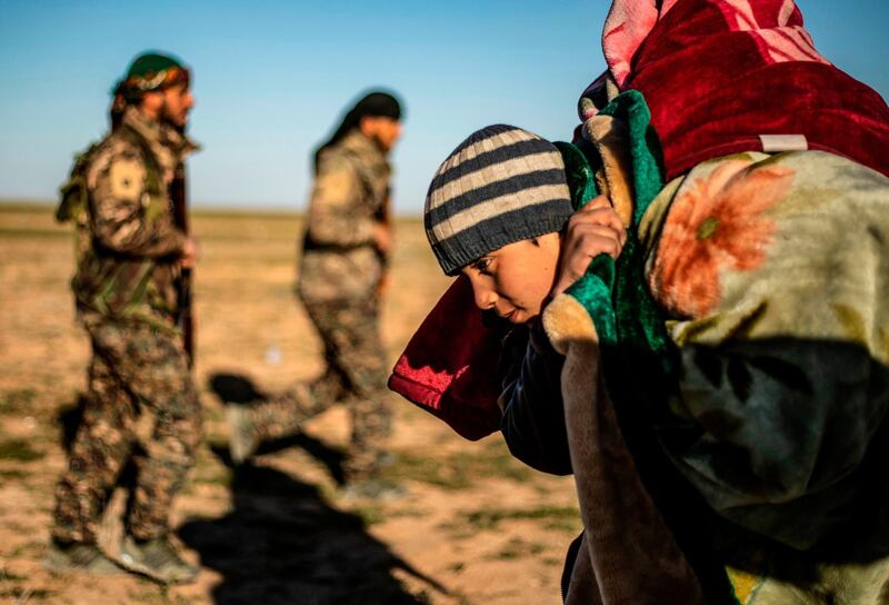 A child walks carrying covers on his back past members of the Kurdish-led Syrian Democratic Forces (SDF) after leaving the Islamic State (IS) group's last holdout of Baghouz, in the eastern Syrian Deir Ezzor province on March 1, 2019. Kurdish-led forces launched a final assault Friday on the last pocket held by the Islamic State group in eastern Syria, their spokesman said. The "operation to clear the last remaining pocket of ISIS has just started", Mustefa Bali, the spokesman of the US-backed Syrian Democratic Forces, said in a statement using an acronym for the jihadist group. / AFP / Delil SOULEIMAN
