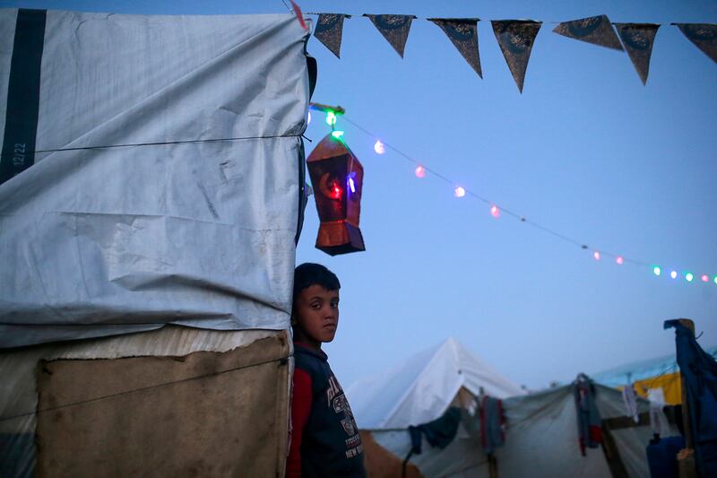 A displaced Palestinian child outside his family's shelter as lanterns and Ramadan accessories decorate the tents. EPA