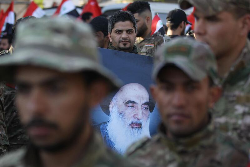 A member of Hashed al-Shaabi holds a picture of Iraq's top Shiite cleric Grand Ayatollah Ali Sistani during the funeral procession of fellow comrades in Baghdad on December 31, 2019, who were killed on the weekend in US air strikes on a base in western Iraq near al-Qaim, on the border with Syria. Iraqi supporters of pro-Iran factions attacked the US embassy in Baghdad, breaching its outer wall and chanting "Death to America!" in anger over weekend air strikes that killed two dozen fighters. It was the first time in years protesters have been able to reach the US embassy, which is sheltered behind a series of checkpoints in the high-security Green Zone.
 / AFP / AHMAD AL-RUBAYE
