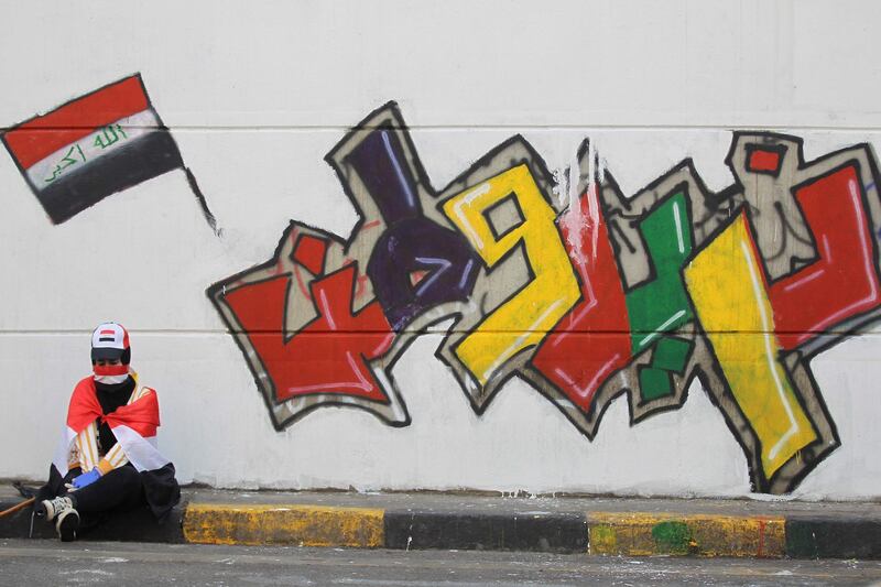 An Iraqi demonstrator clad with the national flag rests in front of a mural which reads "we want a homeland", amid ongoing anti-government protests in the capital Baghdad. AFP