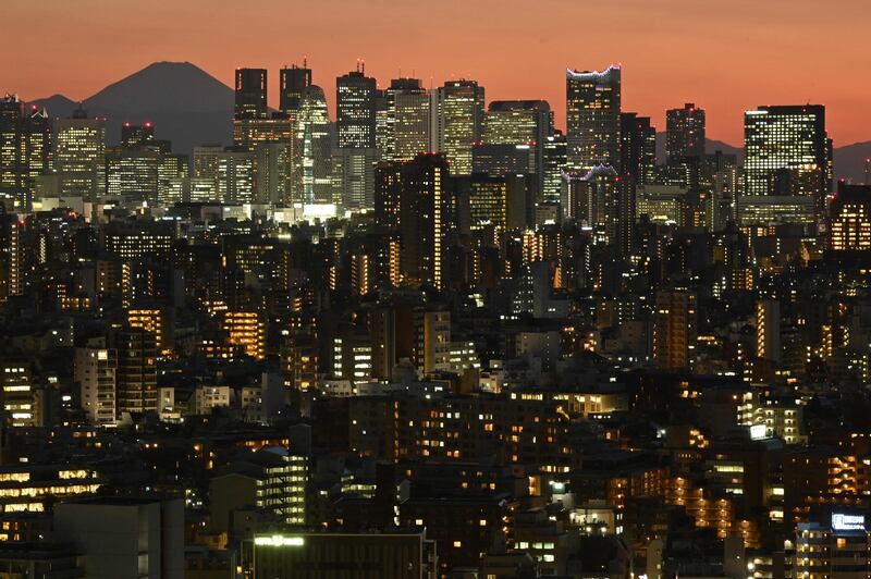 Mount Fuji, Japan's highest mountain, looms behind the illuminated skyscrapers of Shinjuku in Tokyo at sunset. AFP