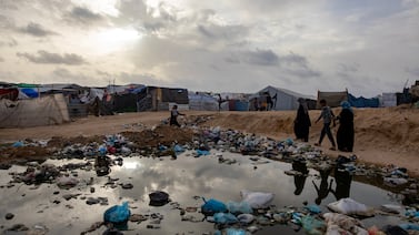 Palestinians walk next to a sewage spill and rubbish near tents for internally displaced people in Rafah. EPA