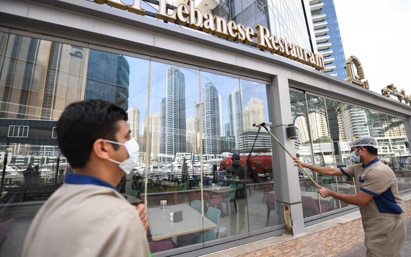 Labourers, wearing protective face masks, disinfect the front of restaurant in Dubai's marina on March 16, 2020. / AFP / KARIM SAHIB
