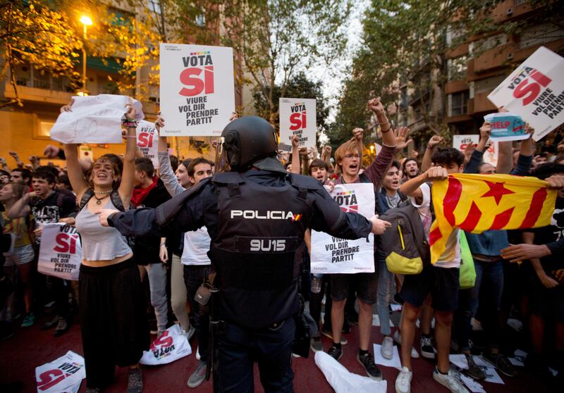 A Spanish national police officer tries to stop demonstrators protesting outside the main offices of the left wing party CUP in Barcelona, Spain, Wednesday, Sept. 20, 2017. Thousands of people supporting a contested referendum to split Catalonia from Spain took to Barcelona's streets amid an intensifying government crackdown on the independence vote that included the arrests of a dozen regional officials Wednesday and the seizure of 10 million ballot papers. (AP Photo/Emilio Morenatti)