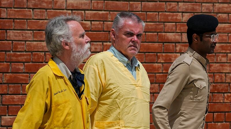 Jim Fitton of Britain, left, and Volker Waldmann of Germany, center, wearing yellow detainees’ uniforms and handcuffed are escorted by Iraqi security forces, outside a courtroom, in Baghdad, Iraq, Sunday, May 22, 2022.  Waldmann and Fitton have been accused of smuggling ancient shards out of Iraq.  (AP Photo / Hadi Mizban)