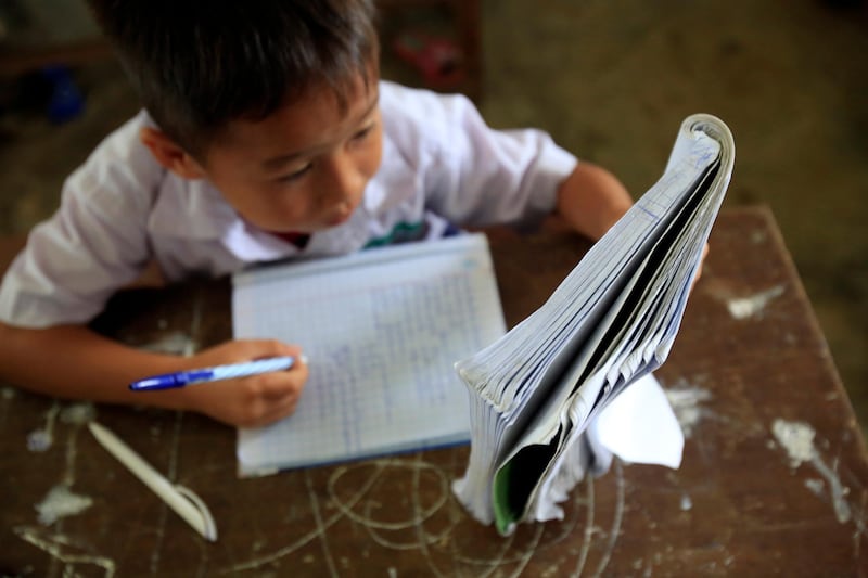 Elementary school. Schoolboy reading textbook in classroom. Vang Vieng, Laos.  (Photo by: Godong/UIG via Getty Images)