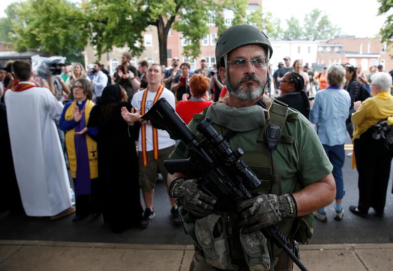A white supremacist militia member stands in front of clergy counter protesting during rally in Charlottesville, Virginia, U.S., August 12, 2017.   REUTERS/Joshua Roberts - RTS1BJKF