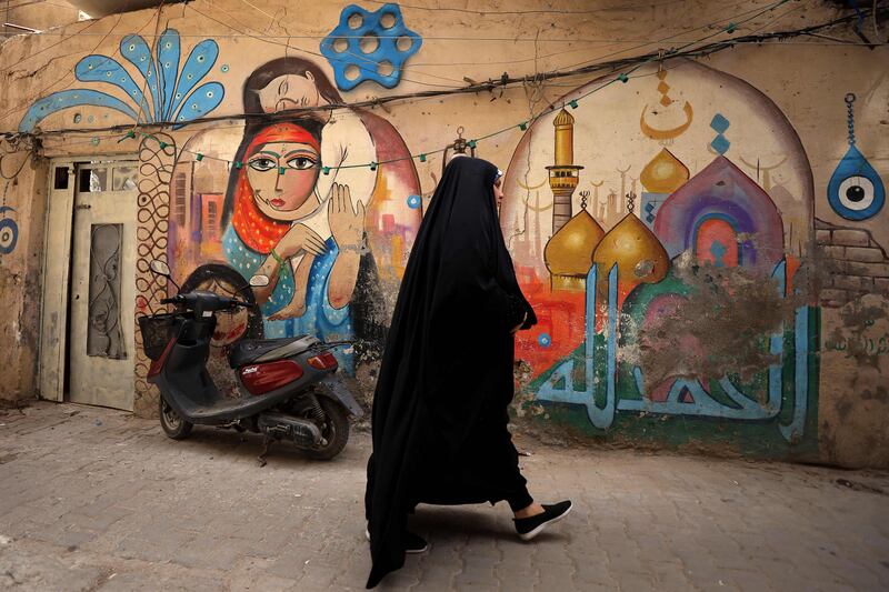 A woman walks past street art in Baghdad's Al Anbari neighbourhood. Iraq's government says its citizens deserve a secure living environment, essential services and a break from conflict. AFP