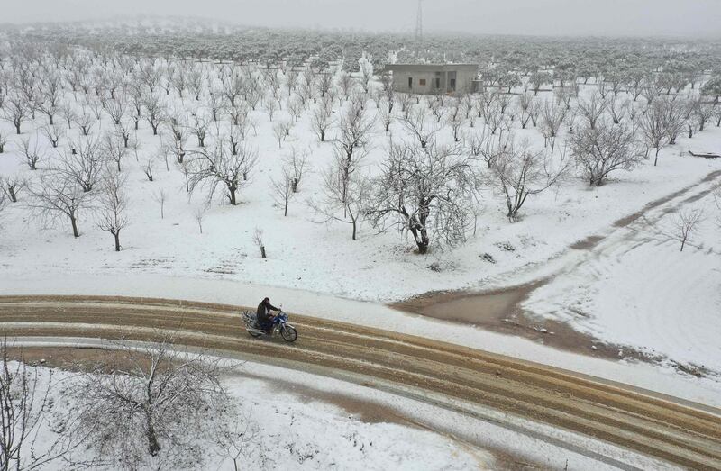 A Syrian man rides a motorcycle among groves covered with snow in the Jabal al-Zawiya region in the rebel-held northern countryside of Syria's Idlib province, on February 17, 2021.  AFP