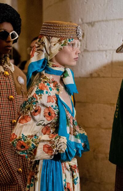 Waiting backstage, a model wears layers of scarves and a woven pill box hat at the Gucci cruise show