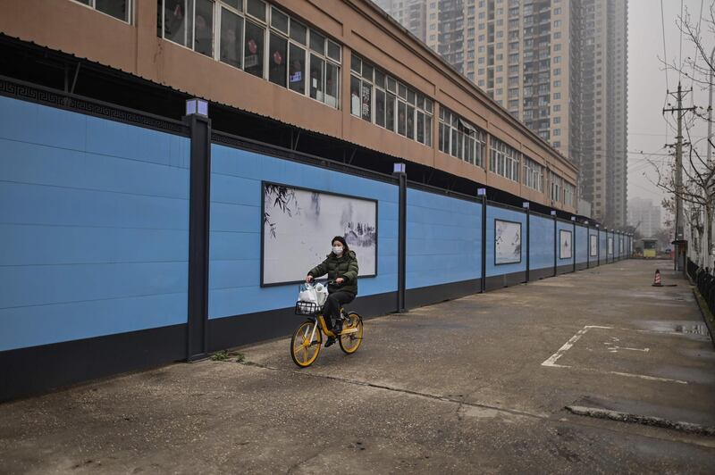 A woman cycles past the closed Huanan Seafood wholesale market in Wuhan, China's central Hubei province on January 23, 2021, one year after the city went into lockdown to curb the spread of the Covid-19 coronavirus. / AFP / Hector RETAMAL
