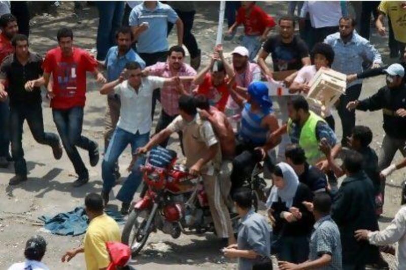 Egyptian protesters beat a man as he tries to escape on the back of a motorcycle after he was accused of attacking demonstrators in the Abbassiya district in Cairo today. At least 12 people were killed when attackers stormed an antimilitary protest near the Defence Ministry in Cairo, medics and a security official said. The fate of the man is unknown.