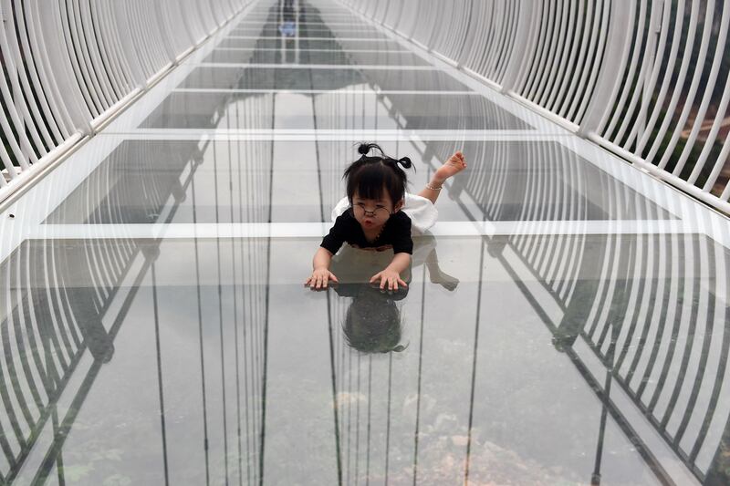 A young visitor crawls on the Bach Long glass bridge in Moc Chau district in Vietnam's Son La province on April 29, 2022.  - Vietnam launched a new attraction for tourists -- with a head for heights -- on April 29 with the opening of a glass-bottomed bridge suspended some 150 metres above a lush, jungle-clad gorge.  (Photo by Nhac NGUYEN  /  AFP)
