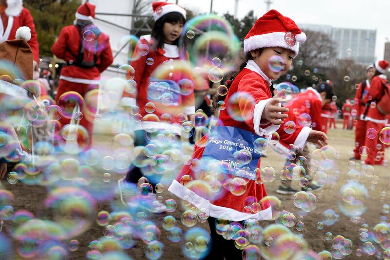 A girl dressed in a Santa Claus costume plays with bubbles prior to the Tokyo Great Santa Run 2018. EPA