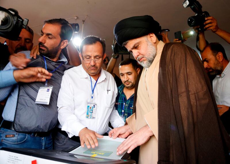 Iraqi Shiite cleric and leader Moqtada al-Sadr (C-R) puts his ballot through an electronic counting machine into a ballot box at poll station in the central holy city of Najaf on May 12, 2018 as the country votes in the first parliamentary election since declaring victory over the Islamic State (IS) group. Polling stations opened at 7:00 am for the roughly 24.5 million registered voters to cast their ballots across the conflict-scarred nation. / AFP / Haidar HAMDANI
