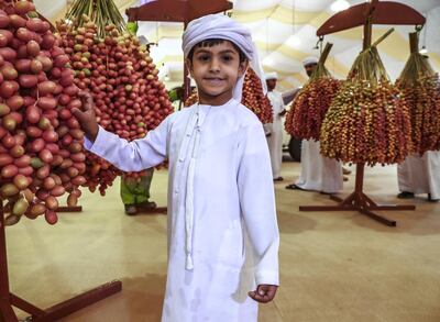 Abu Dhabi, U.A.E., July 18, 2018.  First day of the 2018 Liwa Date Festival. --  Saif Al Mazrouei (6) poses for a souvenir photo beside the heaviest date fruit clumps of the festival.
Victor Besa / The National
Section:  NA
Reporter:  Haneen Dajani