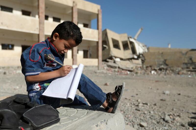 A Yemeni schoolboy writes in a notepad as he sits outside a school that was damaged in an air strike in the southwestern Yemeni city of Taez on March 16, 2017. Ahmad Al Basha / AFP Photo