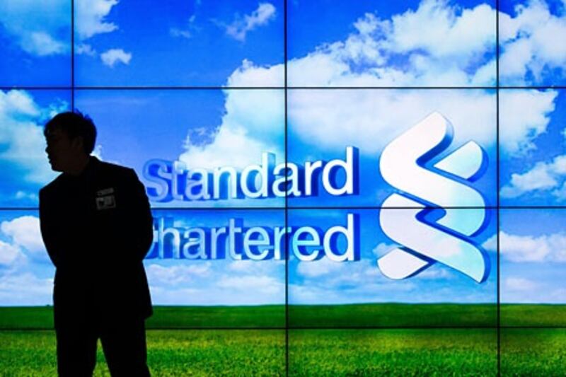 A security guard stands in front of an electronic screen displaying the logo Standard Chartered at a branch of the bank in Hong Kong on March 5, 2013. Standard Chartered was expected to release its 2012 financial results on March 5.  AFP PHOTO / Philippe Lopez

 *** Local Caption ***  622081-01-08.jpg