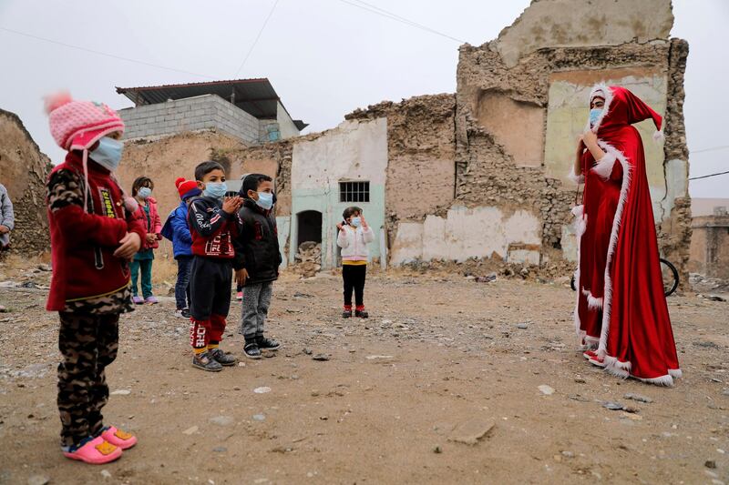 An Iraqi woman, dressed as Santa claus, plays with children, amid the spread of the coronavirus disease in the old city of Mosul, Iraq. Reuters