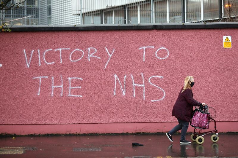 FILE - In this Tuesday, Dec. 8, 2020 file photo, a woman walks past graffiti with the words Victory to the NHS (National Health Service) on a wall at the Royal Victoria Hospital, one of several hospitals around Britain that are handling the initial phase of a COVID-19 immunization program, in West Belfast, Northern Ireland. Britain races to vaccinate more than 15 million people by mid-February, and in an effort to ensure vaccines get to the right places at the right times, along with the syringes, alcohol swabs and protective equipment needed to administer them, the government has called in the army. (AP Photo/Peter Morrison, File)