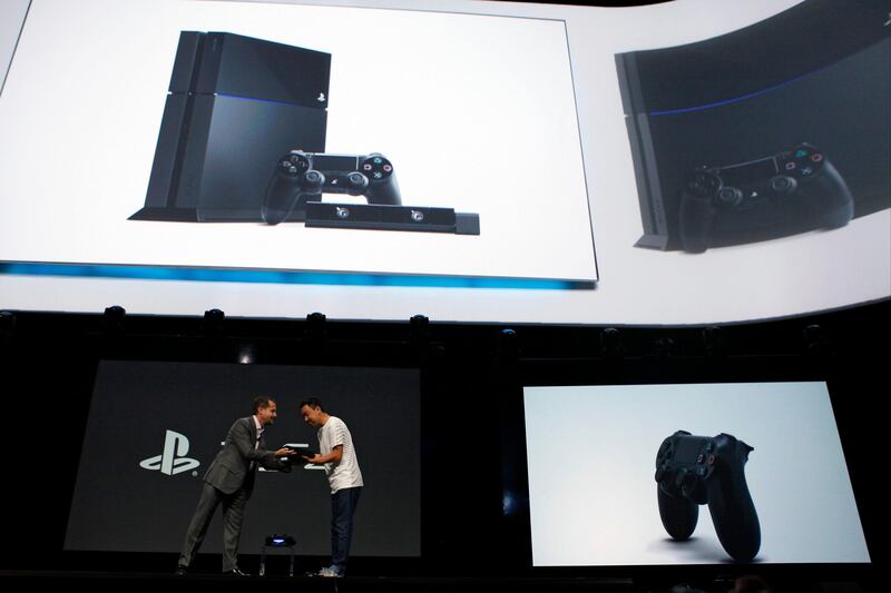 Andrew House, president and group chief executive officer of Sony Computer Entertainment Inc., left, passes the company's PlayStation 4 console to a designer during the Sony Corp. E3 media event in Los Angeles, California, U.S., on Monday, June 10, 2013. Sony Corp. took the wraps off the PlayStation 4, its first new console in seven years, promising original content and fresh titles will revitalize demand and spark a comeback for the video-game industry it once dominated. Photographer: Patrick T. Fallon/Bloomberg *** Local Caption *** Andrew House 1237341.jpg