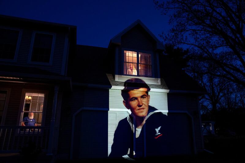 An image of veteran Stephen Kulig, who died from the COVID-19 virus at the age of 92, is projected onto the home of his daughter, Elizabeth DeForest, as she looks out the window of a spare bedroom as her husband, Kevin, sits downstairs in Chicopee, Massachusetts, USA. AP Photo