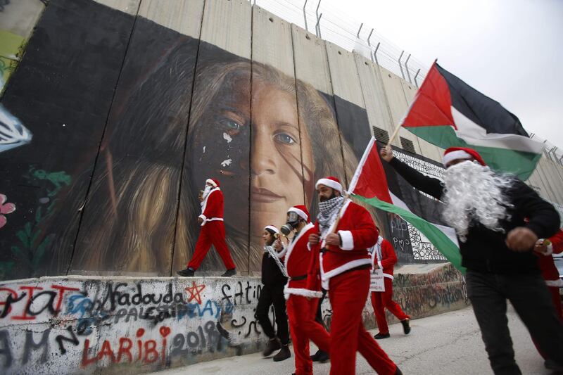Palestinians dressed as Santa Claus in Bethlehem hang signs on a mural painting of militant Ahed Tamimi on Israel's controversial separation barrier in the West Bank. AFP