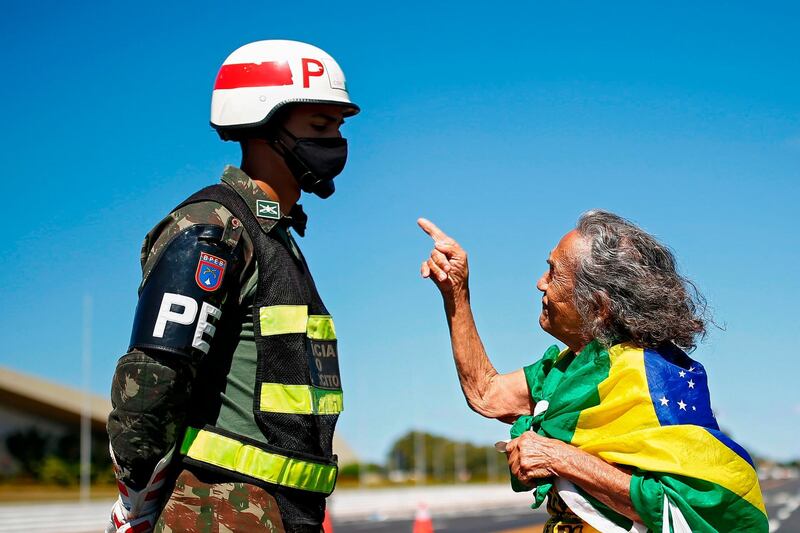 A supporter of Brazilian President Jair Bolsonaro speaks to a soldier as she takes part in a protest outside the army headquarters against the decision of Brasilia's governor to prevent crowds from attending rallies, amid the pandemic, in Brasilia. AFP