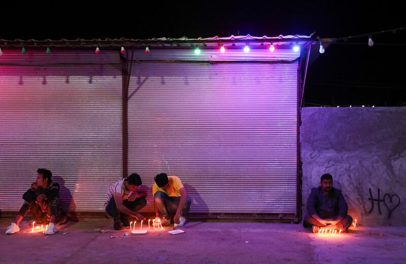 People sit and crouch near lit-up candles as they gather to commemorate the Shiite cleric in the Iraqi city of Karbala on March 28, 2021. Reuters