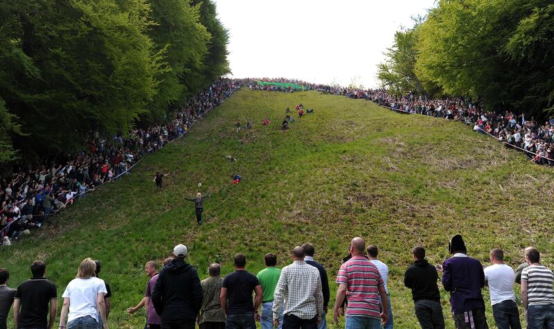 Competitors run down Coopers Hill in pursuit of a fake foam round Double Gloucester cheese during the annual cheese rolling and wake near the village of Brockworth near Gloucester in western England on May 27, 2013. With a disputed history dating back to at least the 1800s, the annual Cooper's Hill Cheese Rolling involves hordes of fearless competitors chasing an eight pound Double Gloucester cheese down a steep hill. The slope has a gradient in places of 1-in-2 and in others 1-in-1, its surface is very rough and uneven and it is almost impossible to remain on foot for the descent. The winner of the race down the hill wins the cheese. AFP PHOTO/CARL COURT
 *** Local Caption ***  210111-01-08.jpg