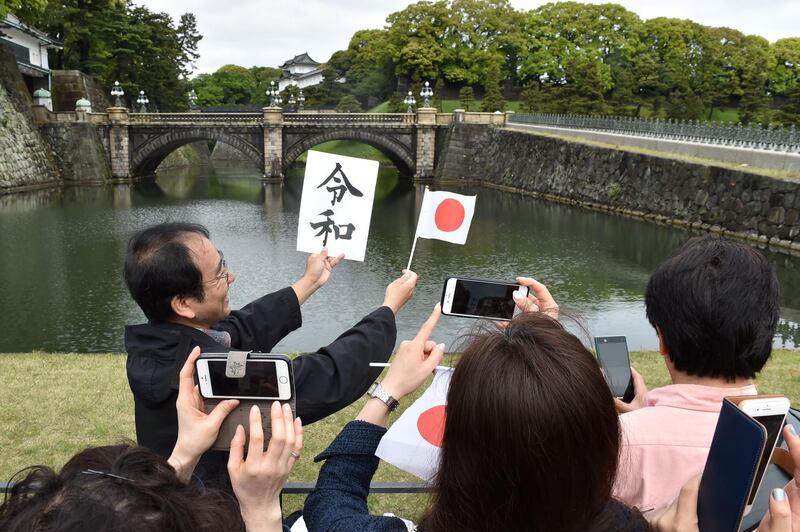 Visitors take photos of a man holding up a Japanese flag along with a card showing the characters for the new "Reiwa" era to mark the new emperor's reign, outside the grounds of the Imperial Palace in Tokyo. Japan's new Emperor Naruhito formally ascended the Chrysanthemum Throne on May 1, a day after his father abdicated from the world's oldest monarchy and ushered in a new imperial era.  AFP