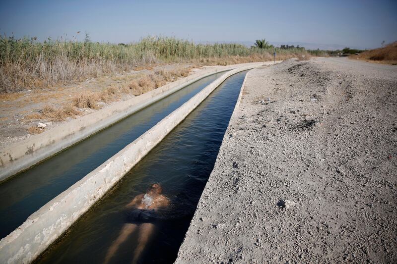 A man cools himself in a water channel at the Beit She'an Valley in Israel. Abir Sultan / EPA