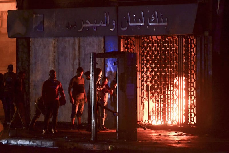 Lebanese anti-government protesters take shelter behind a public phone booth as a local bank's branch burns during clashes with security forces in the northern port city of Tripoli amid fresh protests over a spiralling economic crisis.  AFP