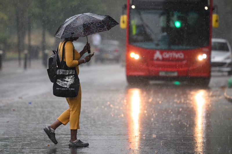 A pedestrian tries to keep dry crossing the road in a very wet London. Getty