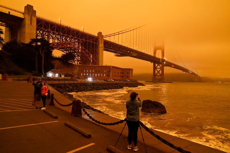 People stop at Fort Point to take morning pictures of the Golden Gate Bridge covered in smoke from wildfires, in San Francisco. AP Photo