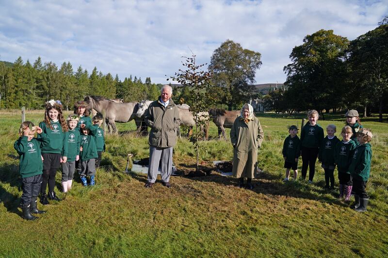 The queen and Prince Charles pose at Balmoral Estate Cricket Pavilion with children from nearby Crathie Primary School, to mark the start of the official planting season for the queen's Green Canopy in October 2021.