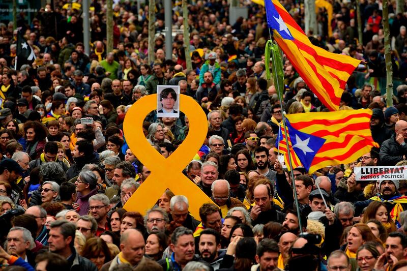 Protesters hold a yellow ribbon with a picture of Catalonia's deposed leader Carles Puigdemont while waving Catalan pro-independence Estelada flags during a demonstration in Barcelona, Spain, on March 25, 2018. Lluis Gene / AFP Photo