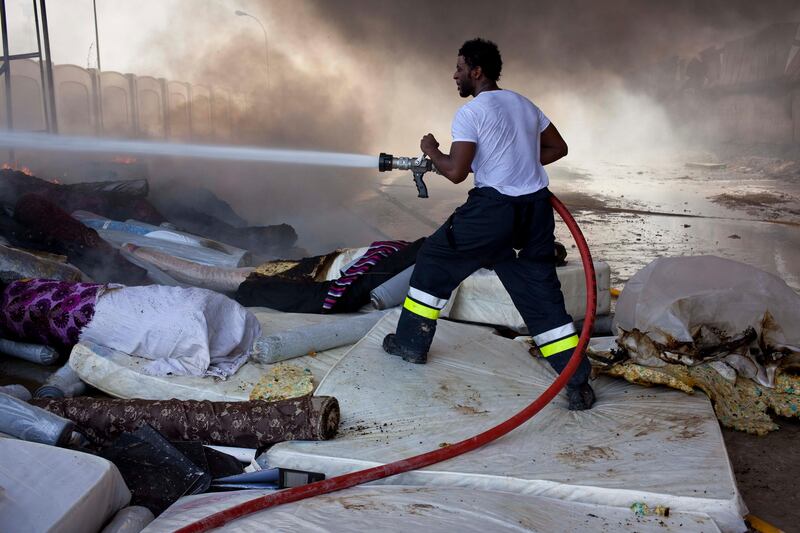 DUBAI, UNITED ARAB EMIRATES,  AUGUST 12, 2013. A fire rages through a car breaker/scrap yard of the Sharjah Industrial area located behing Sharjah City Center. Civil Defense work on dowsing the flames that spread to an adjacent furniture factory. When the blaze initially hit employees tried to save the inventory of the factory by carrying it out on the road. As the blaze spread this also caught fire. (ANTONIE ROBERTSON / The National) Journalist Yassin *** Local Caption ***  AR_1208_Sharjah_Fire13.jpg