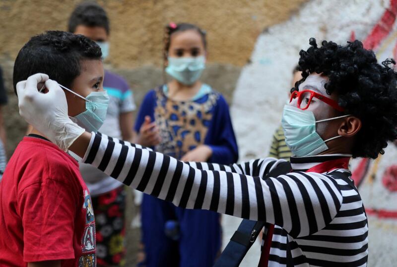 Egyptian clown Ahmed Naser, helps children to put on face masks in Darb Al Ban district at Islamic Cairo, Egypt. Reuters