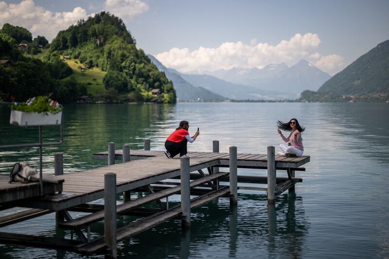 Tourists take photographs on the pier at Iseltwald by the shore of Lake Brienz in the Swiss Alps