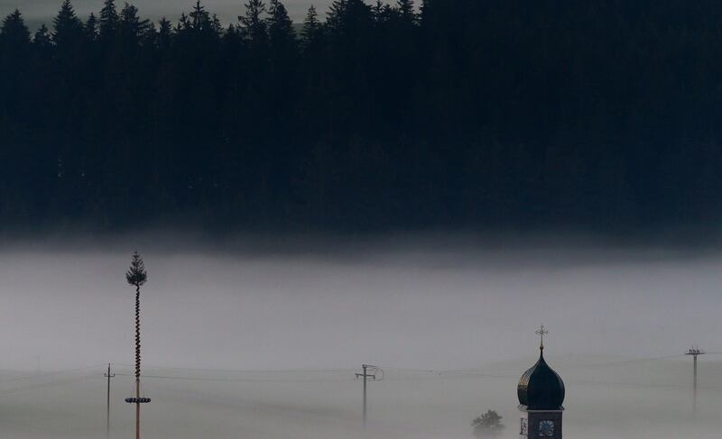 The steeple of the Maria-Hilf pilgrimage chapel and a maypole are surrounded by morning mist in Eisenberg, Germany. Karl-Josef Hildenbrand / dpa / AFP