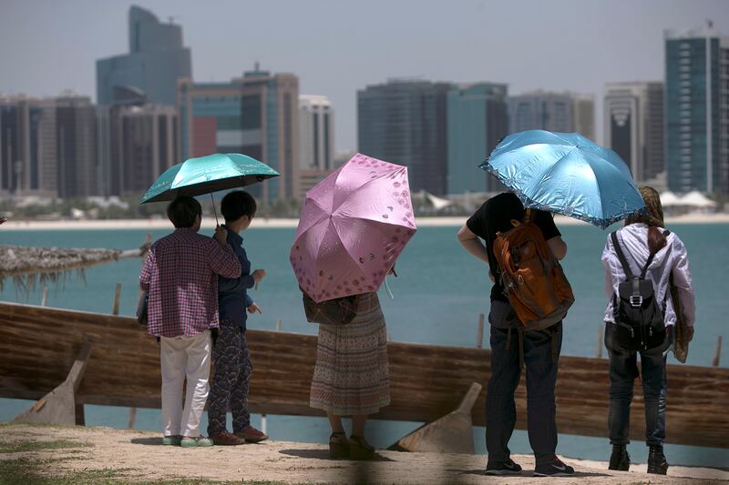 Abu Dhabi, UNITED ARAB EMIRATES, June 5, 2014:  
A group of Chinese tourists shield themselves from the mid-day sun heat, as they visit the Breakwater Corniche in Abu Dhabi, on Thursday, June 5, 2014.
(Silvia Razgova / The National)

Reporter: standalone
Section: National
Usage: June 5, 2014
