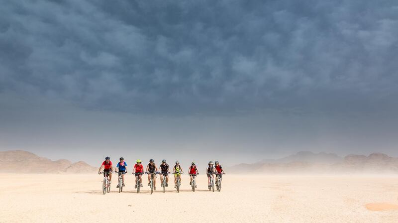 A Group of experienced Mountainbikers is enjoing the ride in the Jordan desert on a driet out lake. Due to the heavy winds during a thunderstorm the air is full of sand but the sunlight is gaining more and more the mastery.