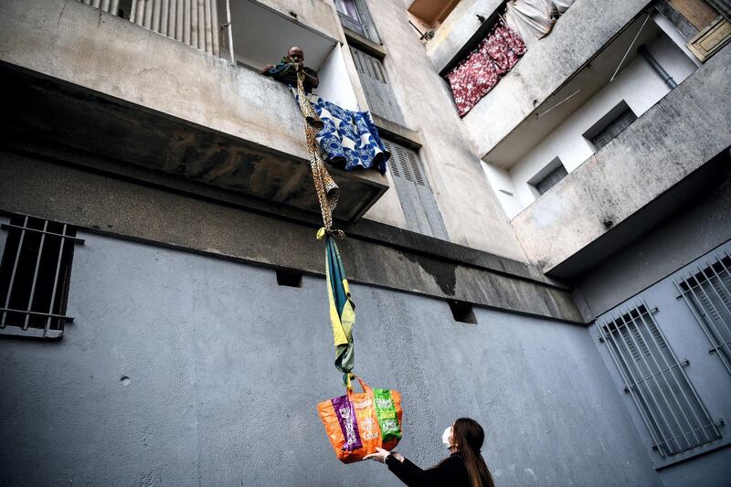 An inhabitant of the residence Maison Blanche (White House residence), composed of 226 mostly unsanitary dwellings, collects food offered by neighbours from his balcony, using a rope made with blankets, on March 31, 2020, in Marseille, southern France, on the fifteenth day of a lockdown aimed at curbing the spread of the COVID-19 (novel coronavirus). (Photo by Anne-Christine POUJOULAT / AFP)