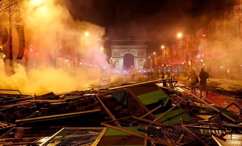 Pedestrians walk amongst extinguished burning material near The Arc de Triomphe on the Champs Elysees in Paris, on November 24, 2018, during a rally by yellow vest protestors against rising oil prices and living costs. Security forces in Paris fired tear gas and water cannon on November 24 to disperse protesters. Several thousand demonstrators, wearing high-visibility yellow jackets, had gathered on the avenue as part of protests which began on November 17, 2018. / AFP / FRANCOIS GUILLOT
