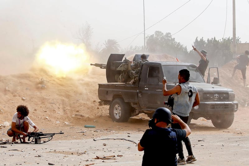 TOPSHOT - A fighter loyal to the Libyan internationally-recognised Government of National Accord (GNA) fires a heavy machine gun as a press photographer take pictures of the scene during clashes against forces loyal to strongman Khalifa Haftar, on May 25, 2019, in the Airport Road Area, south of the Libyan capital Tripoli. / AFP / Mahmud TURKIA
